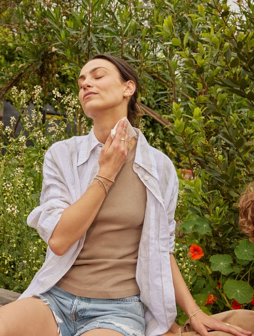 Woman with dark hair applies a Kinfield Golden Hour Repellent Wipe to her neck.