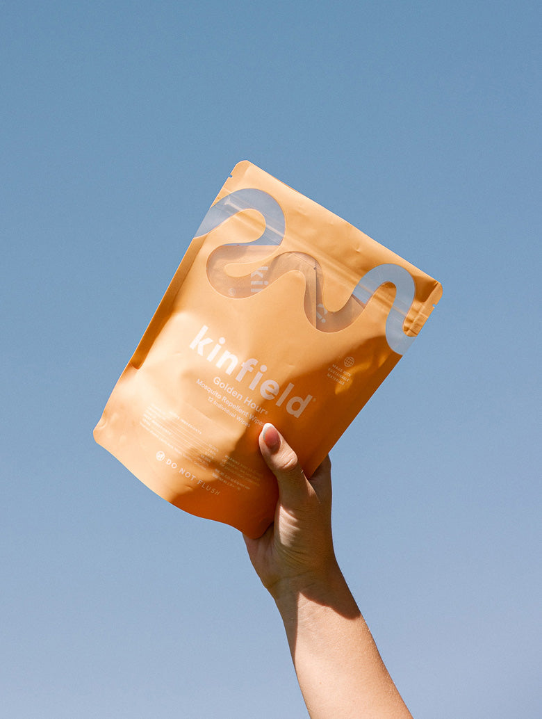 Hand holds a bag of Golden Hour Wipes up in front of a clear blue sky.