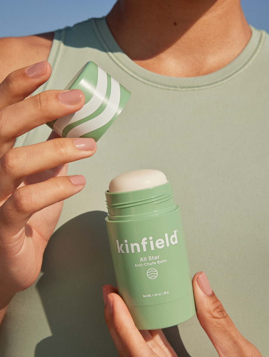 Woman wearing green top opens a tube of Kinfield All Star Anti-Chafe