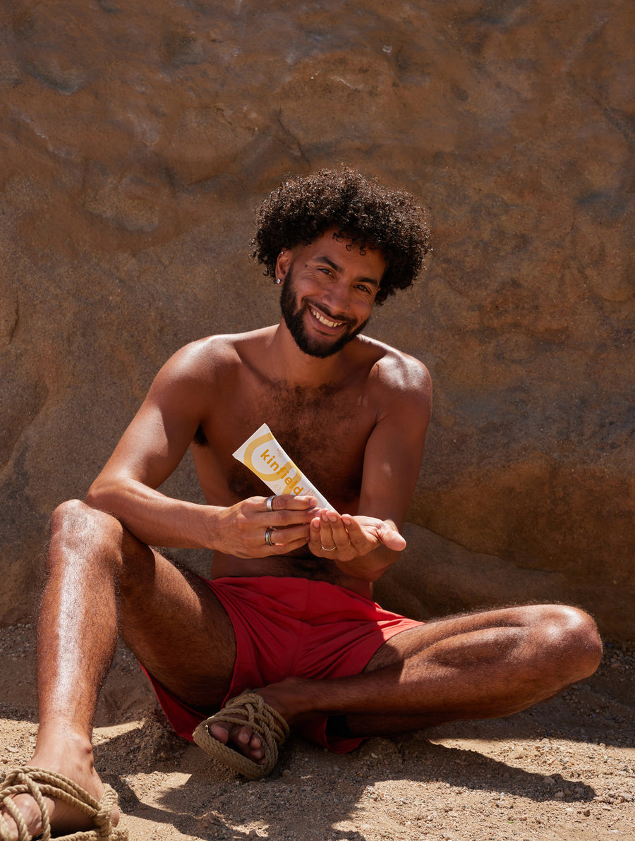 Smiling man with dark curly hair squeezes Kinfield Cloud Cover Sunscreen into his palm on a sunny day.