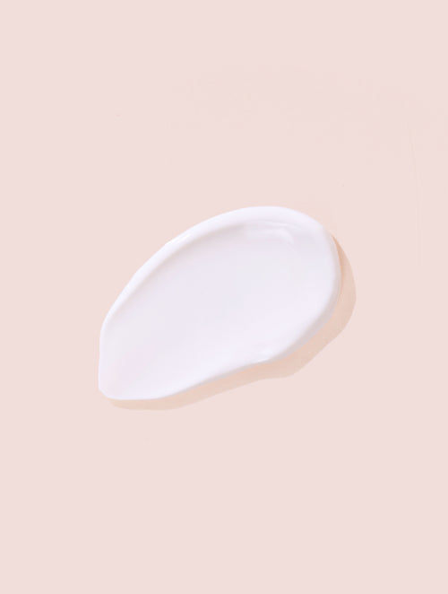 A swatch of white sunscreen lotion on a beigey-peach background