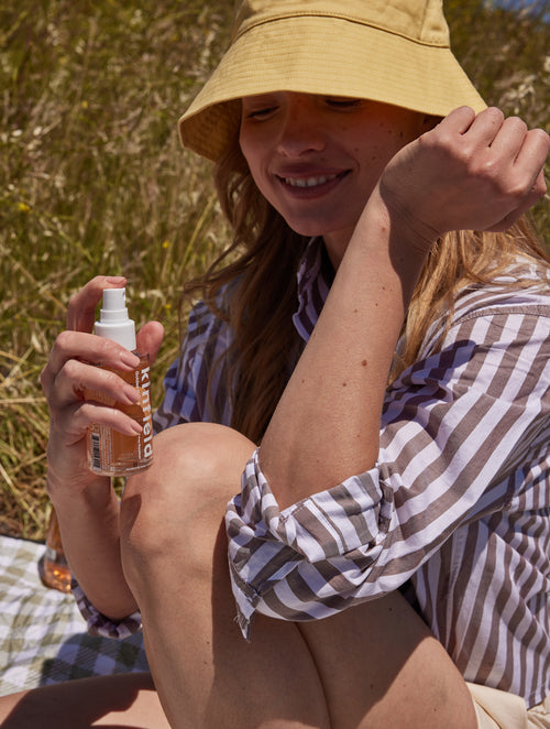 Woman applies Golden Hour Repellent Spray to her arm while outside.